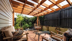 An outdoor patio with wooden furniture, a glass table, and a wooden swing chair. - Auckland Golden Phoenix Holiday Homes (Auckland)