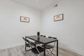 Une salle de conférence avec une grande table en bois foncé, quatre chaises noires et deux œuvres d’art encadrées accrochées aux murs.
