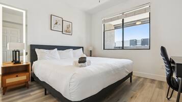 A modern hotel room with a large bed, a desk, and a window with a city view.