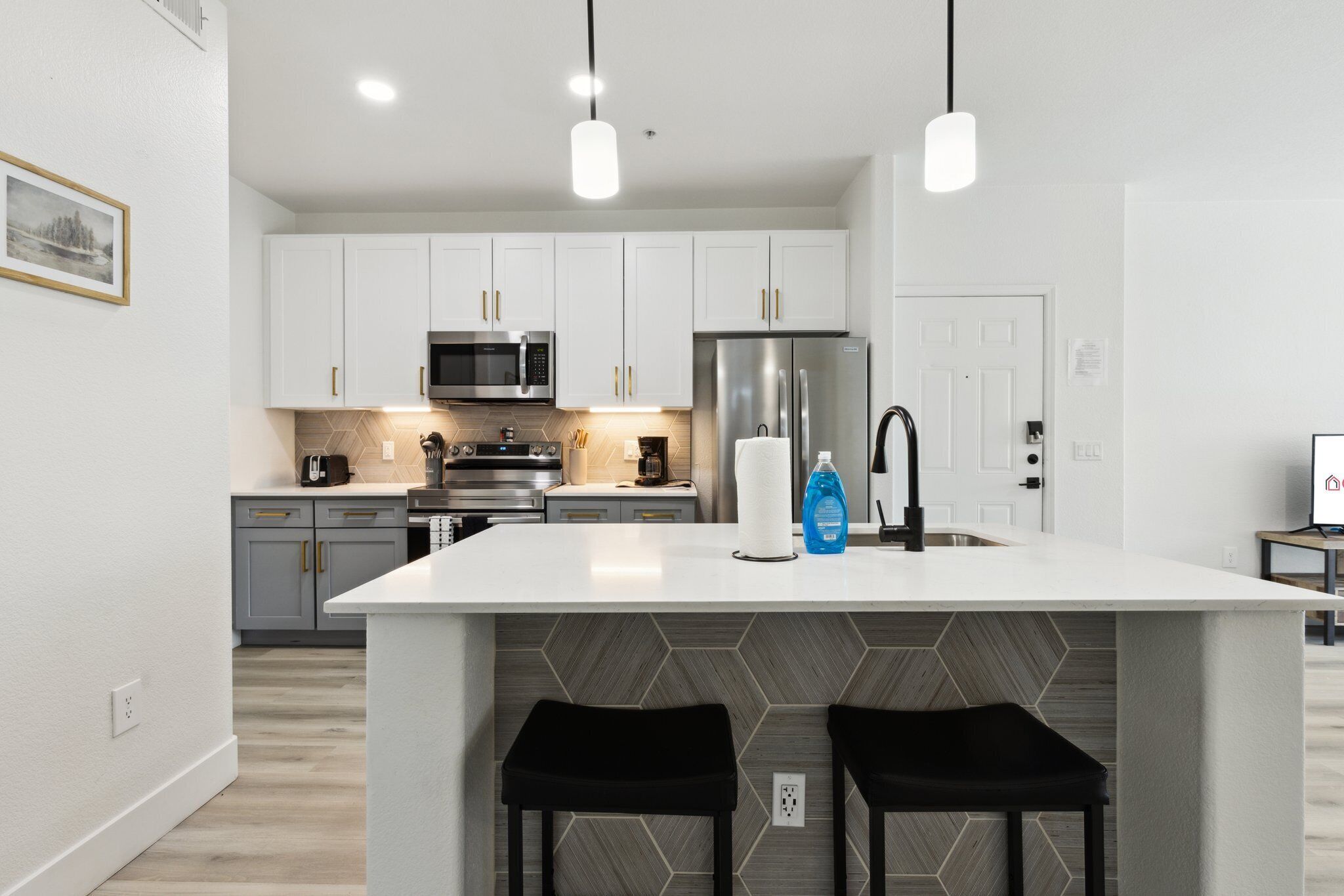 A modern kitchen with white cabinets, a stainless steel refrigerator, and a central island with two black stools.