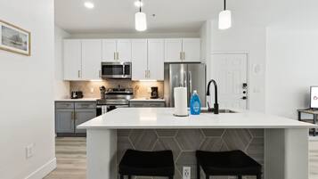 A modern kitchen with white cabinets, a stainless steel refrigerator, and a central island with two black stools.