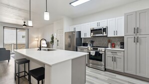 A modern kitchen with white cabinets, stainless steel appliances, and a central island with stools. - CozySuites at Zone Westgate (Glendale)