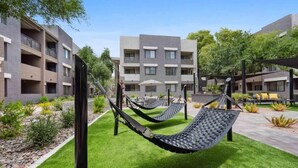 A courtyard with two hammocks, a pool, and a building with balconies. - CozySuites at Zone Westgate (Glendale)