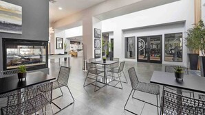 A spacious indoor area with a pool table, seating area with chairs, and large windows offering views of the gym. - CozySuites at Zone Westgate (Glendale)