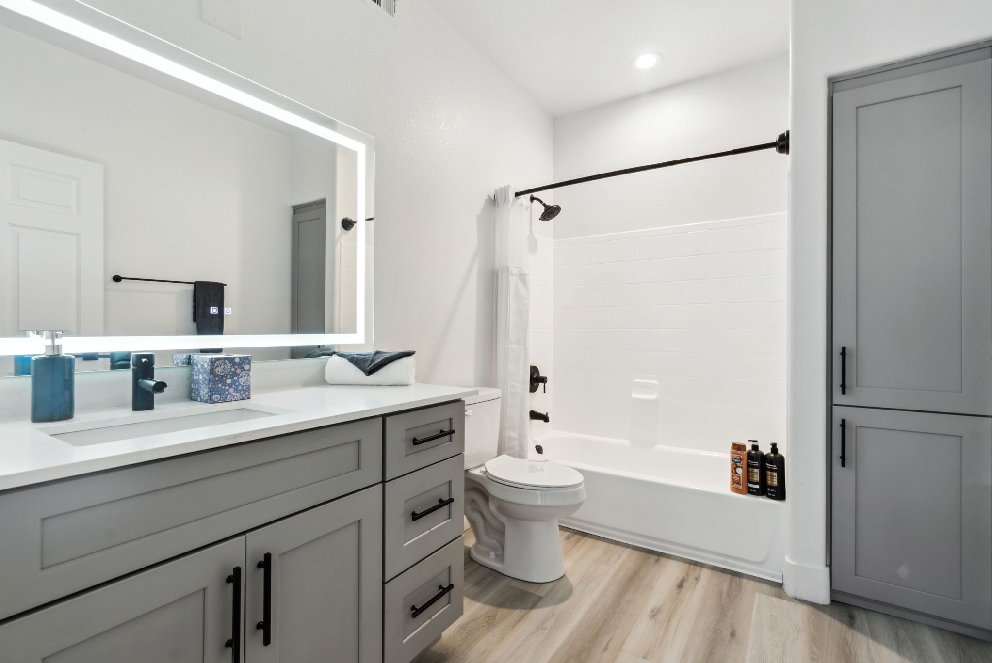 Une salle de bain moderne avec un grand miroir, des toilettes blanches, une baignoire et des meubles gris.