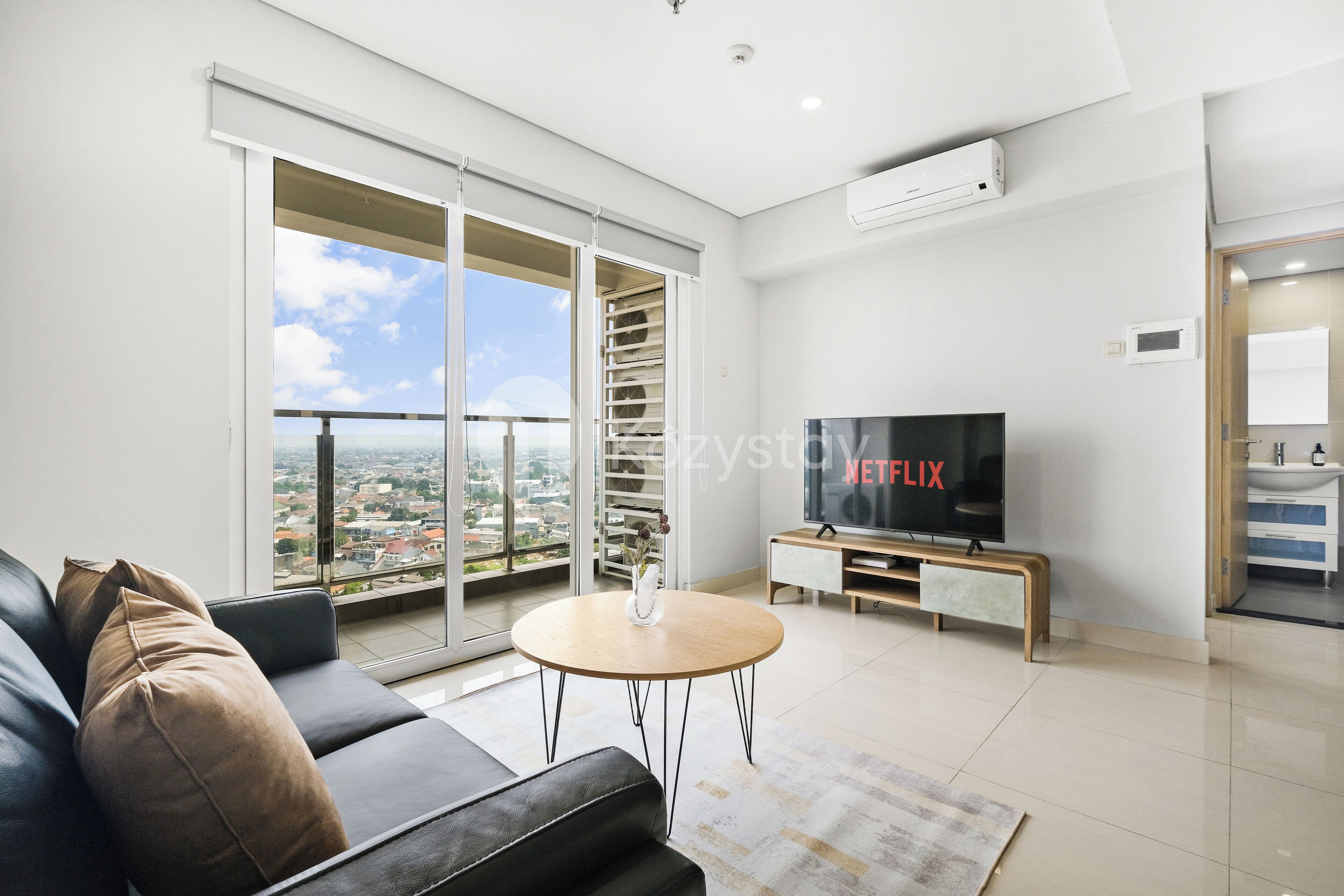 A modern living room with a black leather sofa, a round wooden coffee table, and a large flat-screen TV.