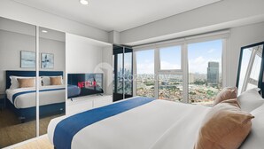 A modern hotel room with a large bed, a TV, and a city view. - Magnolia Aparthotel by Kozystay - Kebon Jeruk (Jakarta)