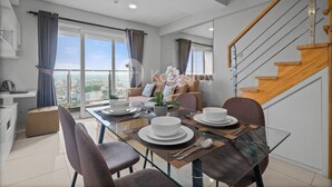 A modern dining area with a glass table, chairs, and a view of the city. - Magnolia Aparthotel by Kozystay - Kebon Jeruk (Jakarta)
