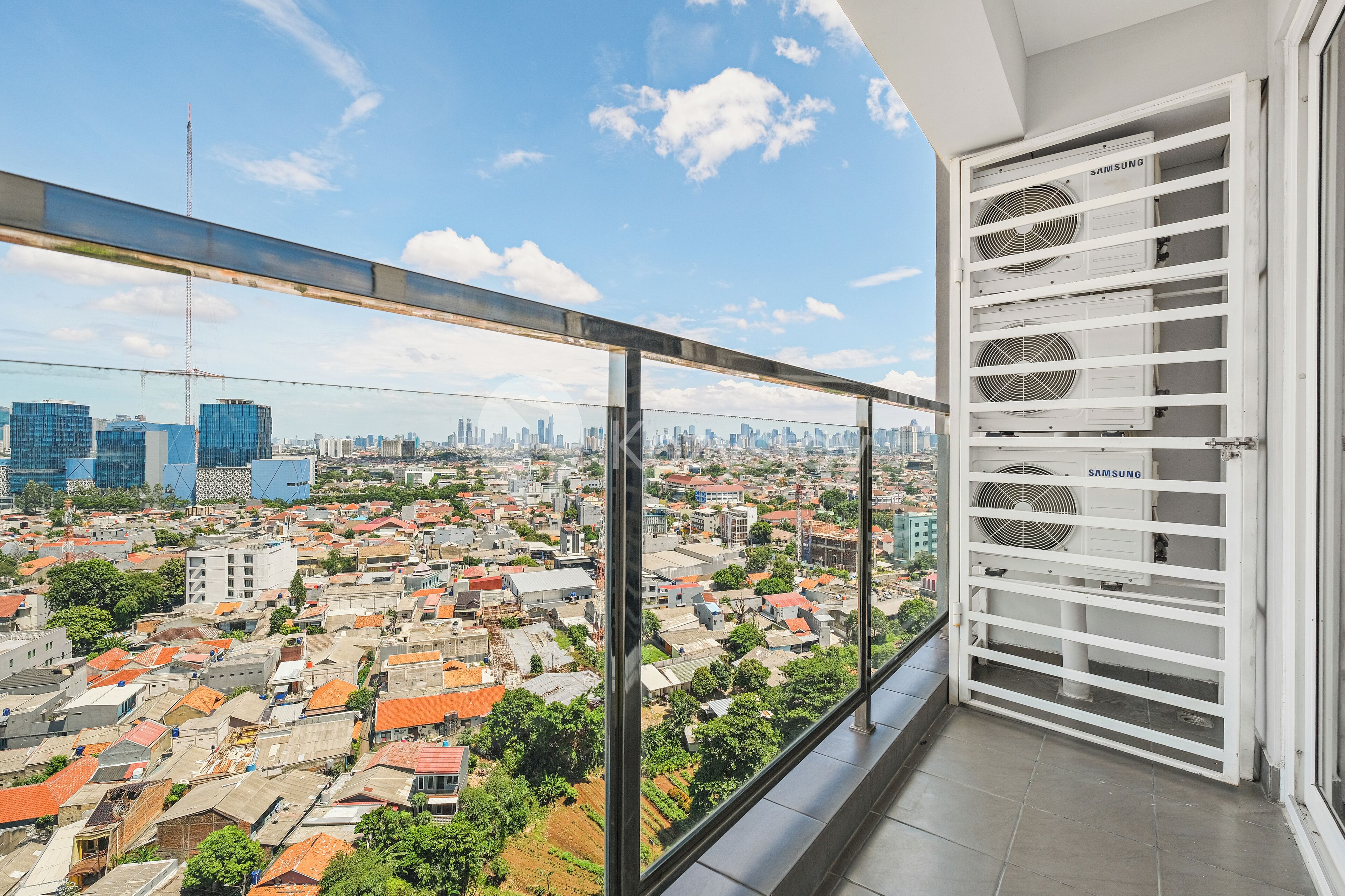 A balcony with a city view, white Samsung air conditioning units, and a metal railing.