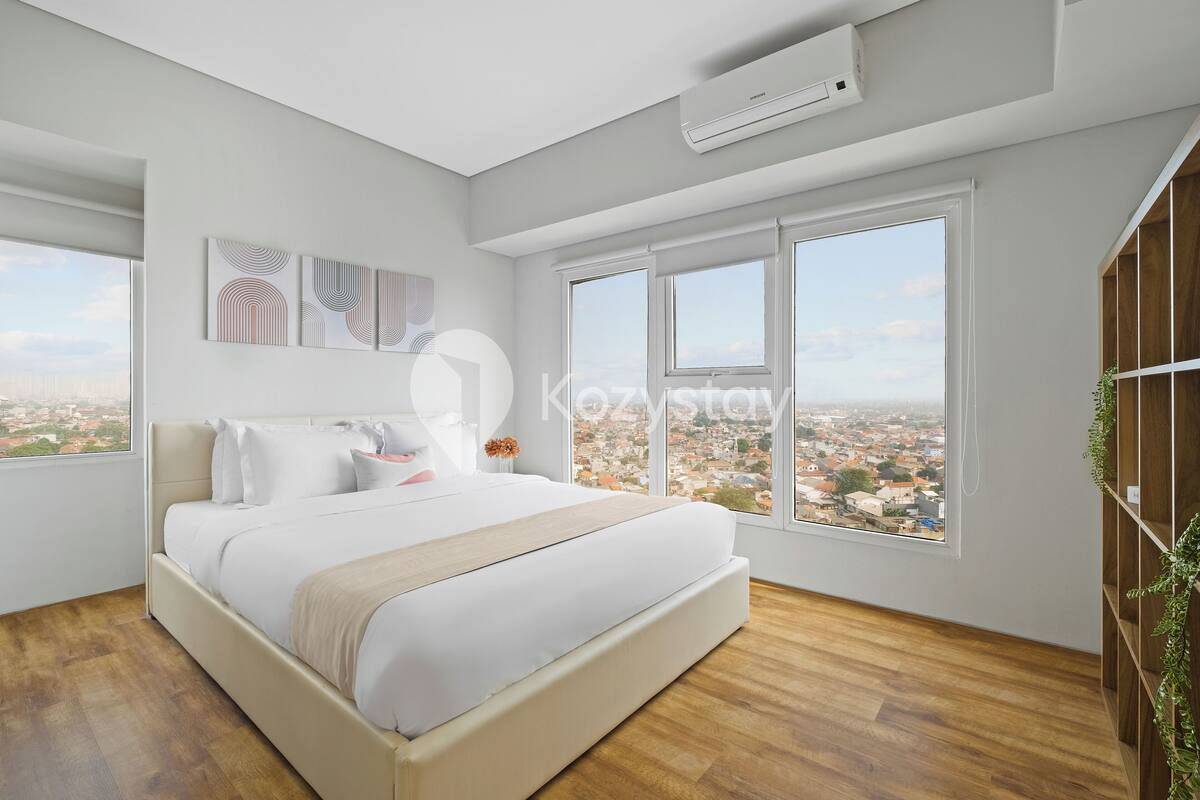 Une chambre moderne avec un grand lit, du linge de lit blanc et une vue sur la ville à travers de grandes fenêtres.