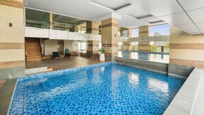 A modern indoor swimming pool with a tiled floor, a staircase leading to a balcony, and a view of the cityscape. - Magnolia Aparthotel by Kozystay - Kebon Jeruk (Jakarta)