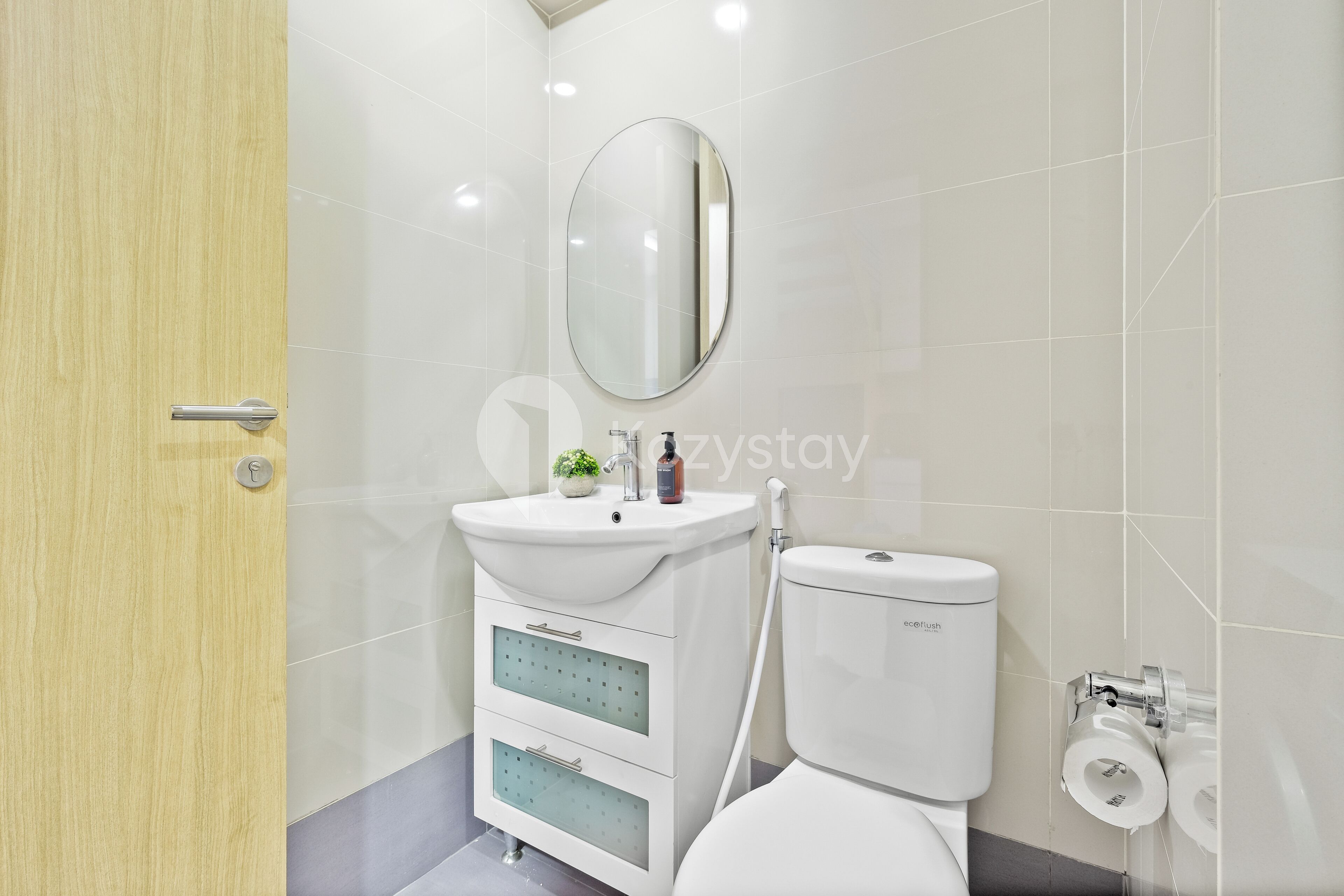 A modern bathroom with a wooden door, a white sink with a mirror, and a toilet.