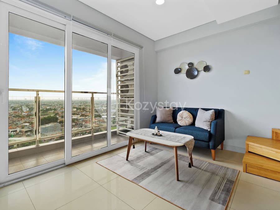 A spacious living room with a large sliding glass door leading to a balcony, a blue sofa, a coffee table, and a wooden bench.