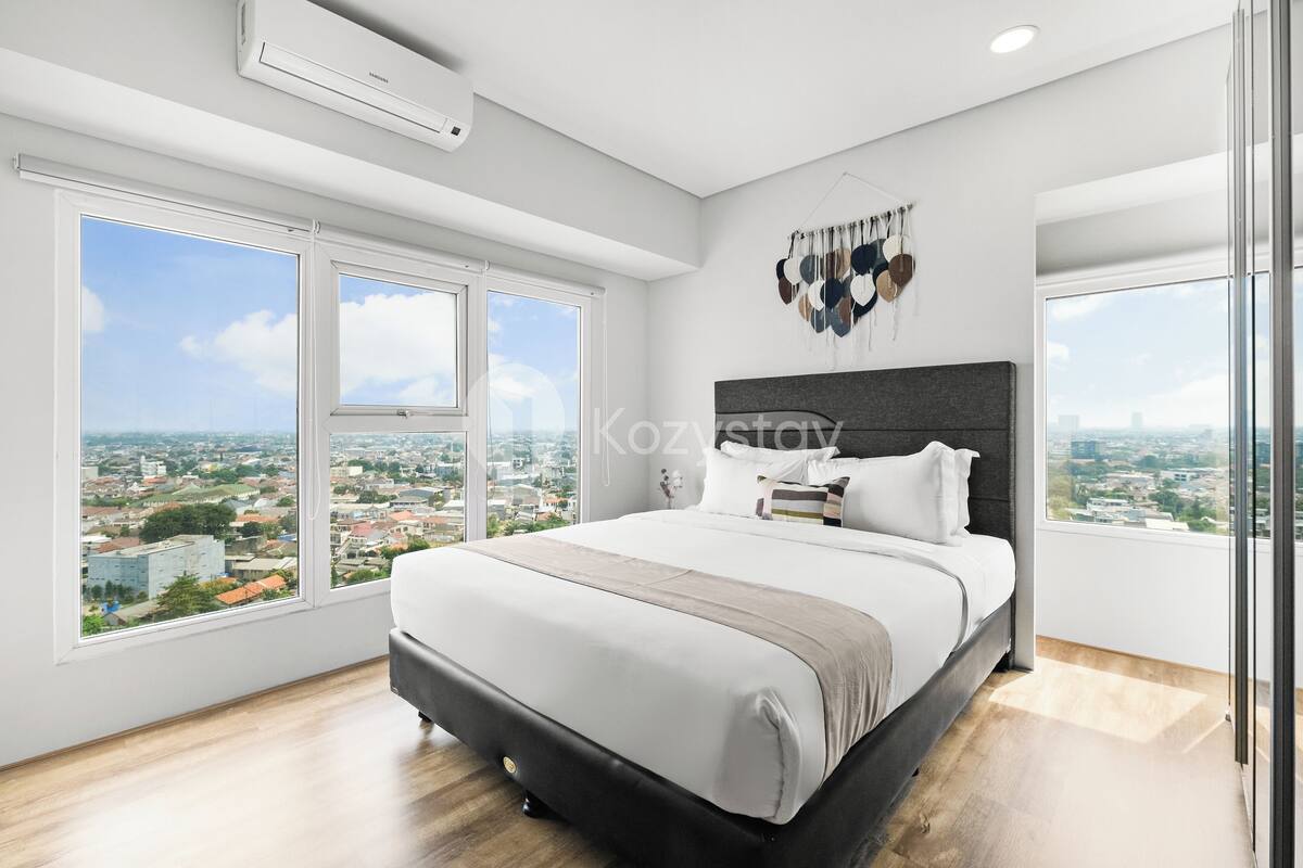 Une chambre moderne dotée d’un grand lit, offrant une vue sur la ville grâce à de larges fenêtres, et agrémentée d’une décoration murale originale.