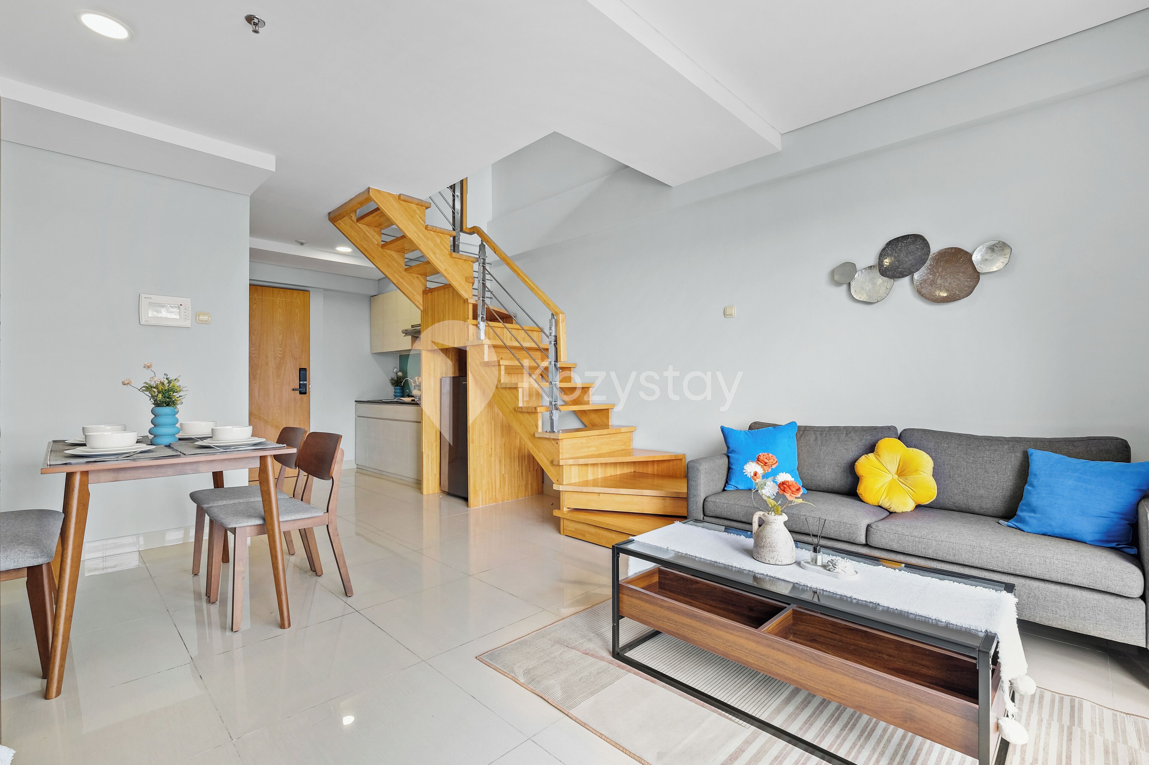 A modern living room with a staircase, a dining area, and a sofa with decorative pillows.