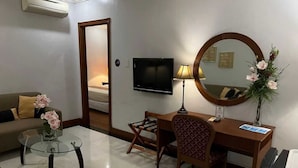 A hotel room with a sofa, a glass coffee table, a desk with a chair, a television, a lamp, a mirror, and a flower arrangement. - VIP Hostel, Evangelista, Makati Manila, Near PNR Pasay (Makati)