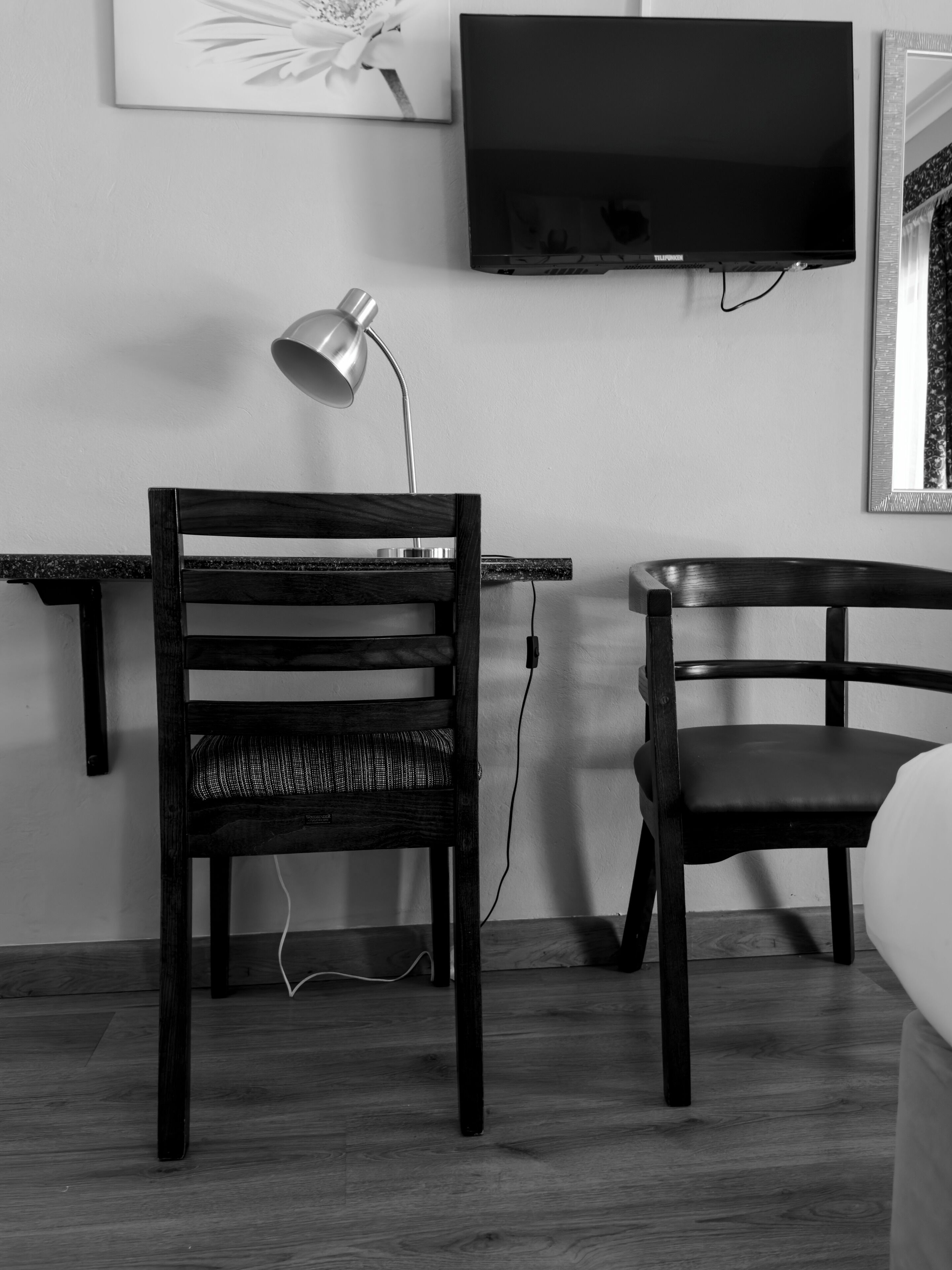 Quarto com escrivaninha, duas cadeiras, luminária, televisão e espelho.