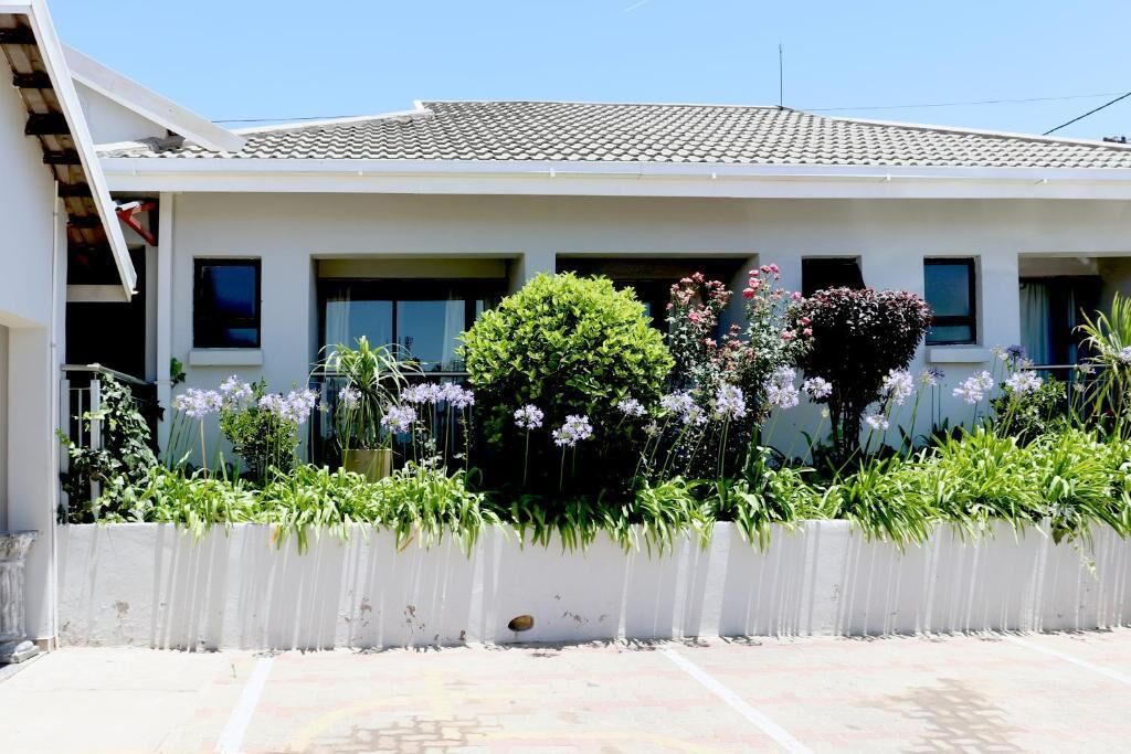 Una casa de dos pisos con techo de tejas, fachada blanca y un jardín con diversas plantas y flores.