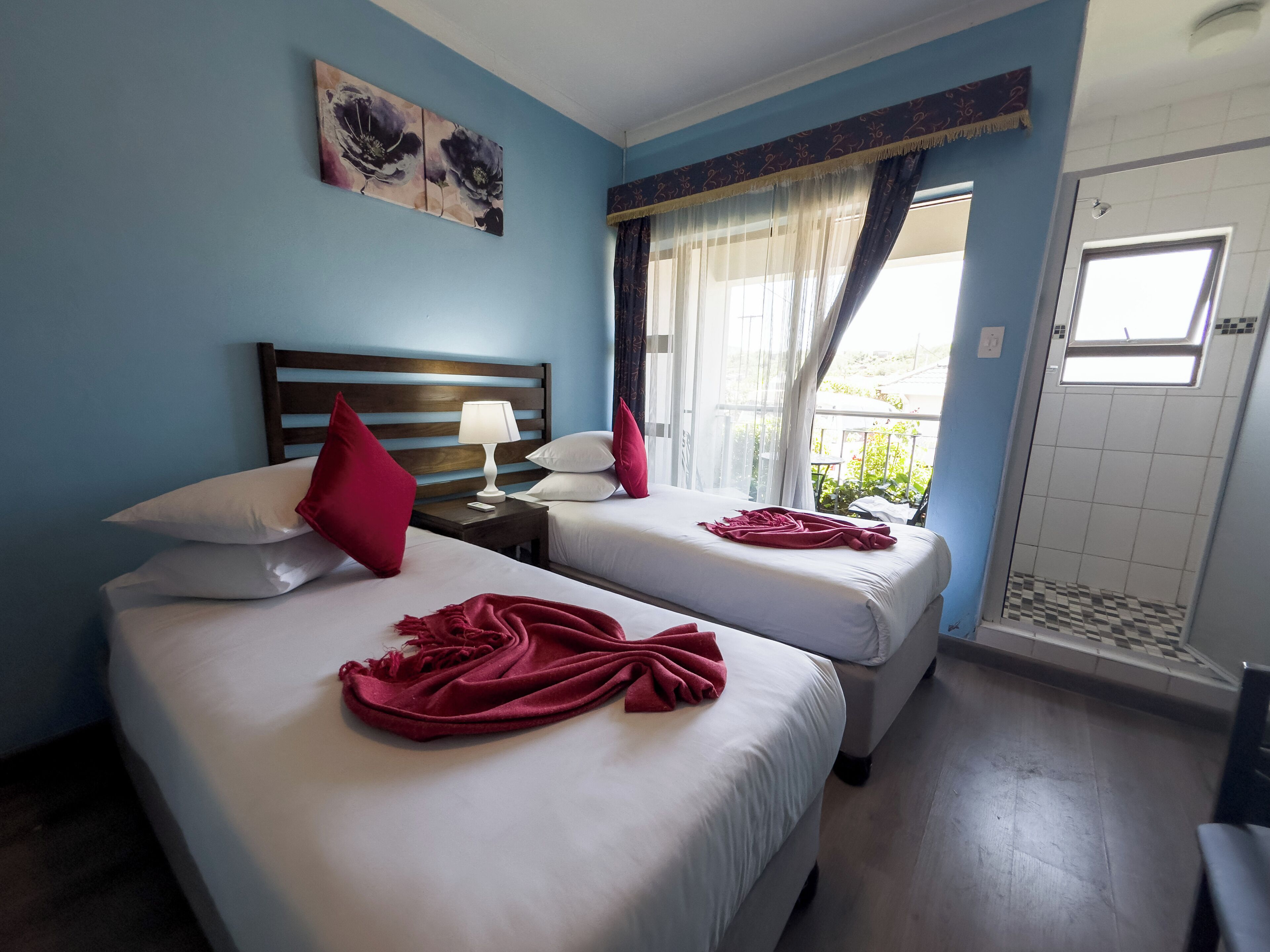 Une chambre d’hôtel avec deux lits, une tête de lit en bois, une table de chevet avec une lampe et une fenêtre avec des rideaux.