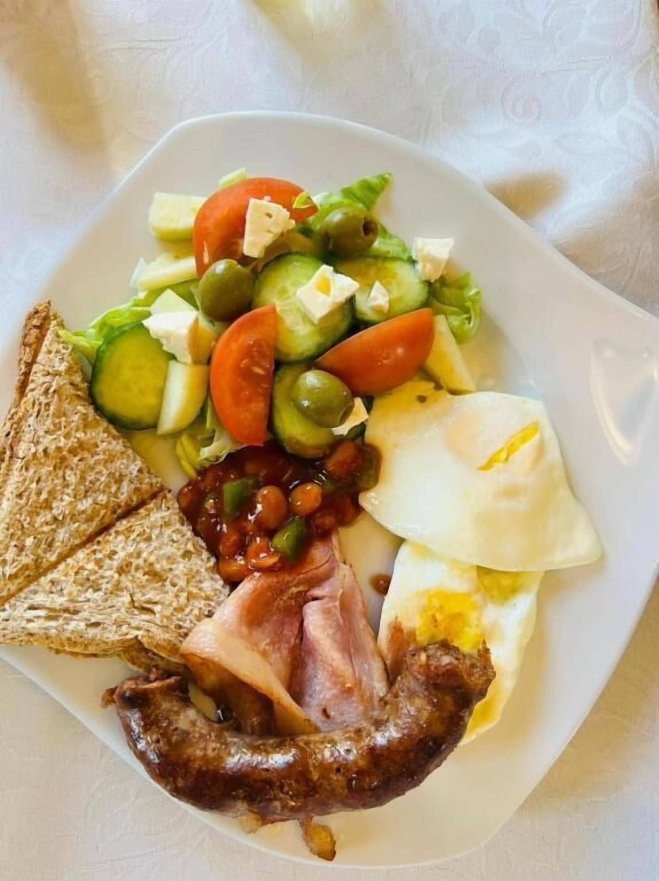 Une assiette garnie de divers aliments pour le petit-déjeuner, notamment des toasts, des œufs, du bacon, des haricots et une salade composée de tomates, de concombres et d’olives.