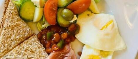 Une assiette garnie de divers aliments pour le petit-déjeuner, notamment des toasts, des œufs, du bacon, des haricots et une salade composée de tomates, de concombres et d’olives.