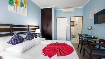 Quarto de hotel com cama, escrivaninha, cadeira, guarda-roupa e banheiro visível por uma porta aberta.