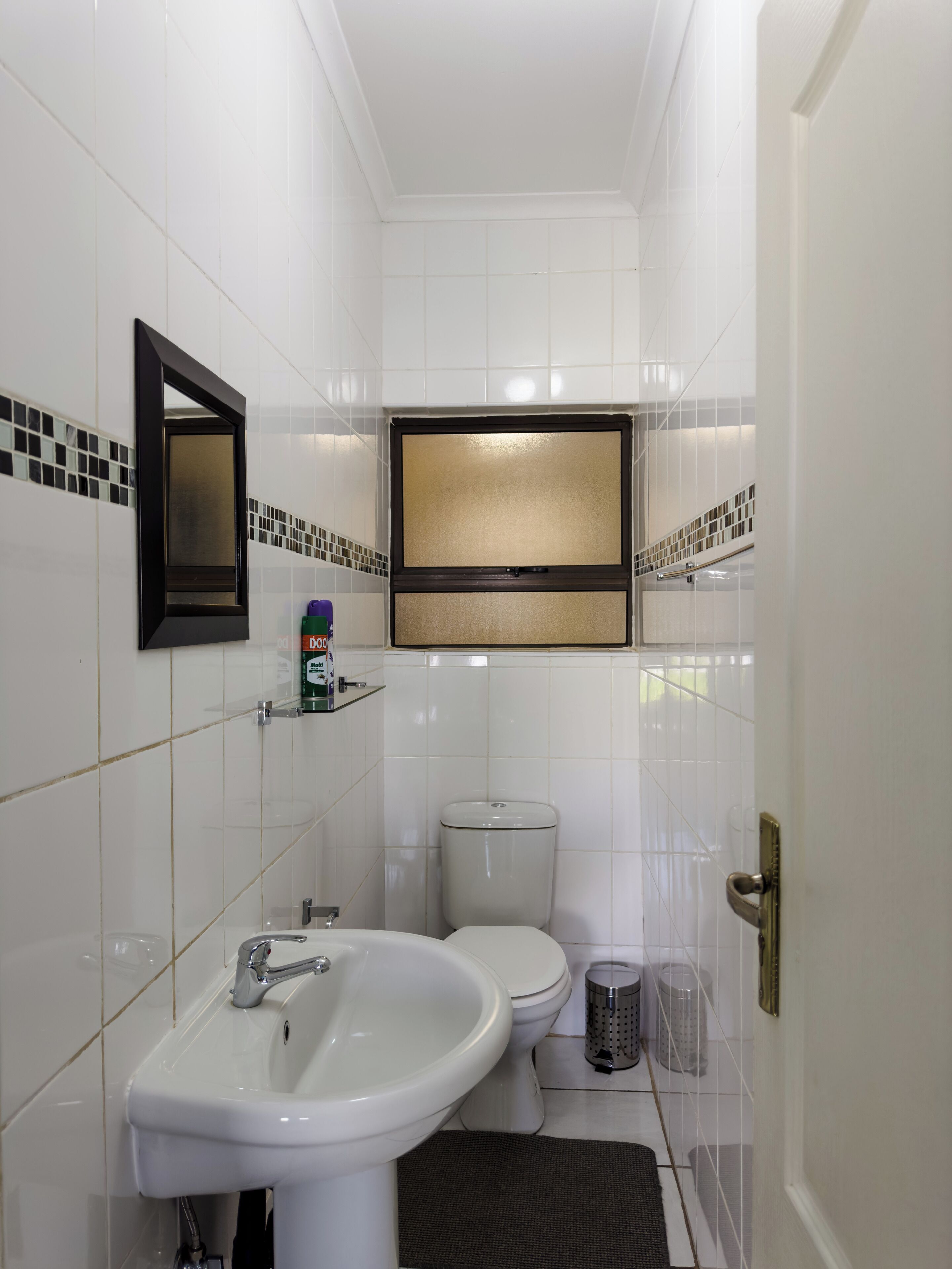 Bagno con piastrelle bianche, lavandino, water, specchio e televisore montato sopra il water.