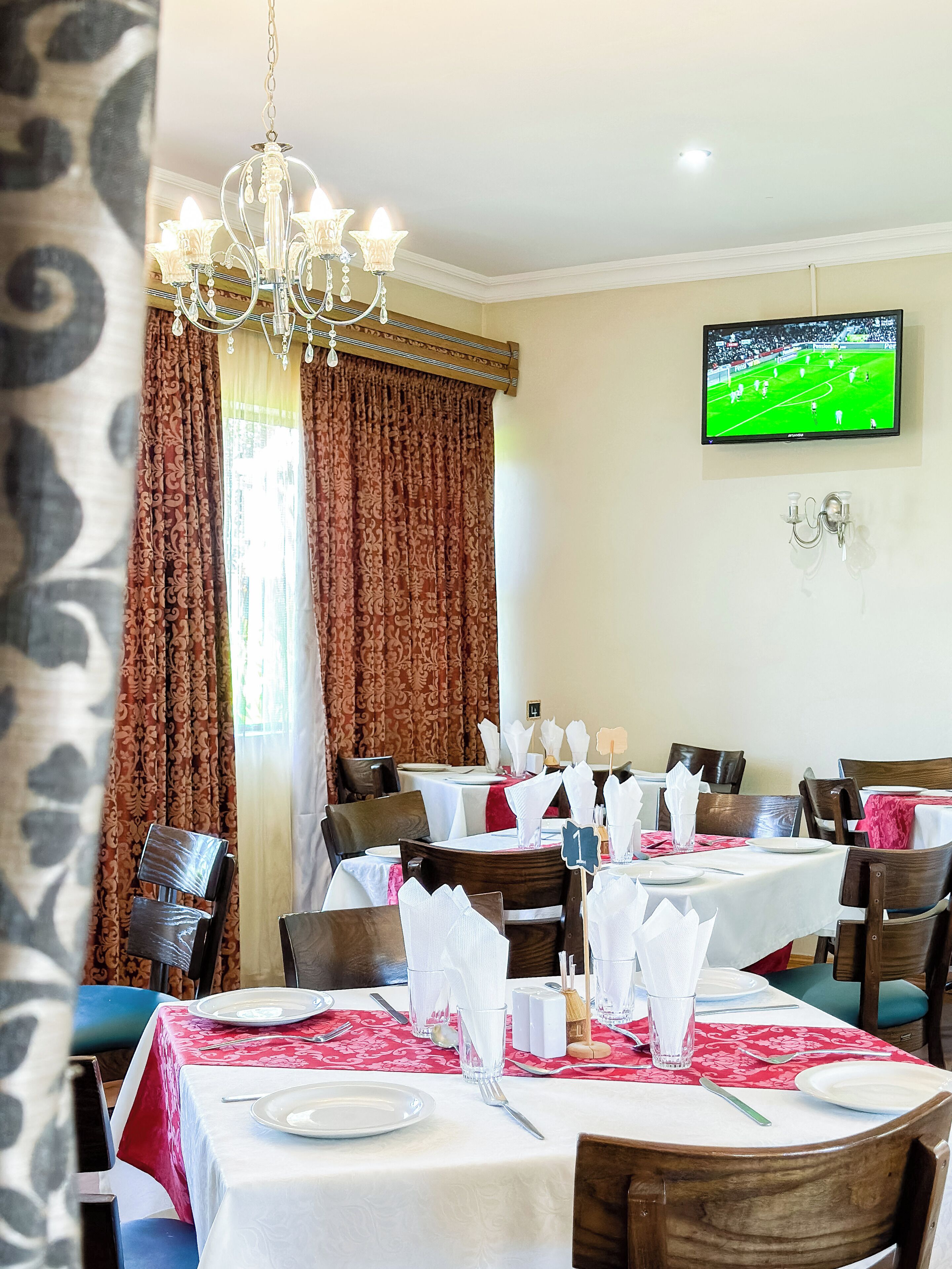 Un comedor con mesas dispuestas para el servicio, una araña y un televisor en la pared.