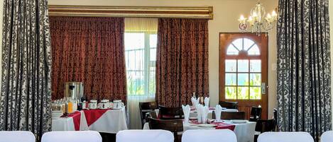 A dining area with tables set for a meal, patterned curtains, and a chandelier.