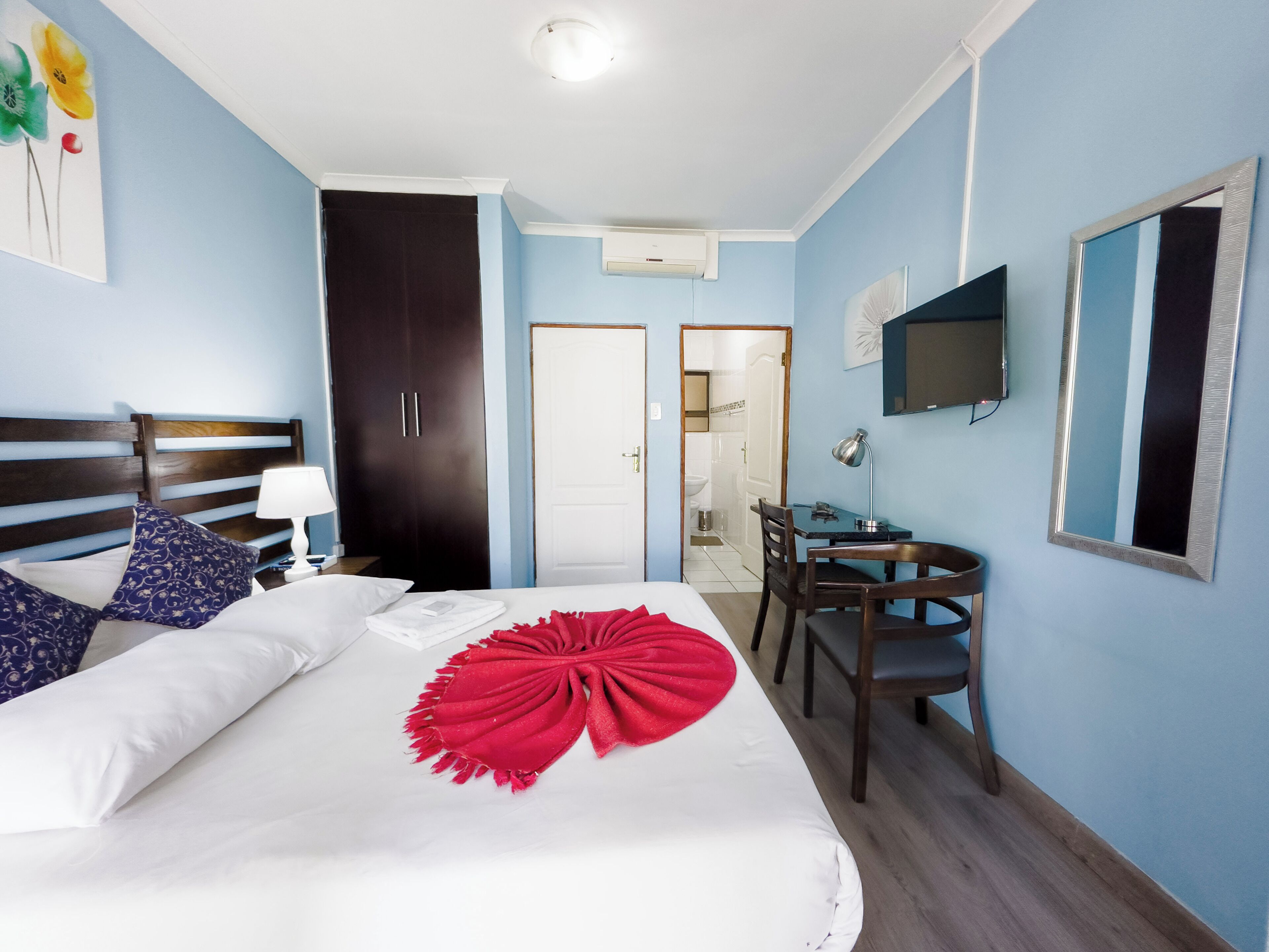 A hotel room with a bed, a desk, a chair, a TV, and a wardrobe.