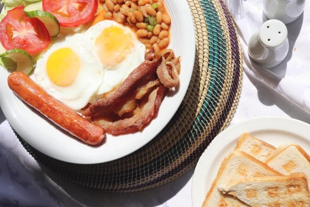Un plato de desayuno con huevos, tocino, frijoles y vegetales.