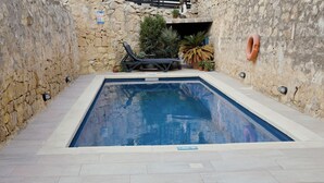 En rektangulär swimmingpool med en stenmur på ena sidan och ett kaklat poolområde med solstolar.