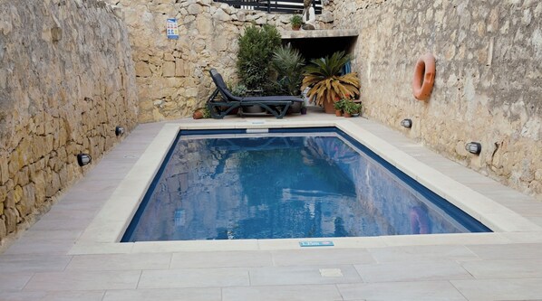 A rectangular swimming pool with a stone wall on one side and a tiled deck area with lounge chairs. - Central House in Sliema with PrivatePool (Sliema)