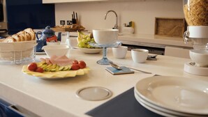 En frukostuppsättning med bröd, ost, tomater och vindruvor på en köksbänk.