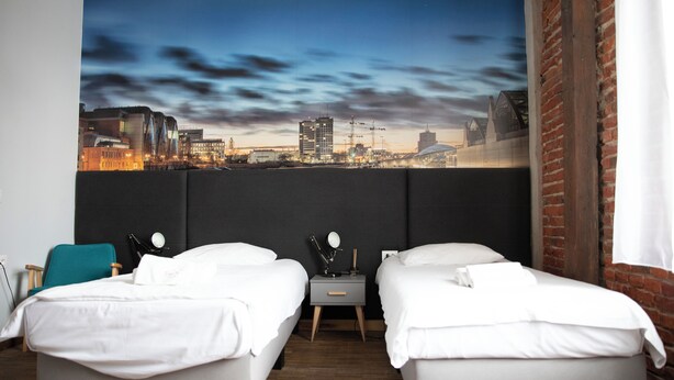A hotel room with two beds, a nightstand, and a cityscape view. - Adler Bed & Breakfast (Lódz)