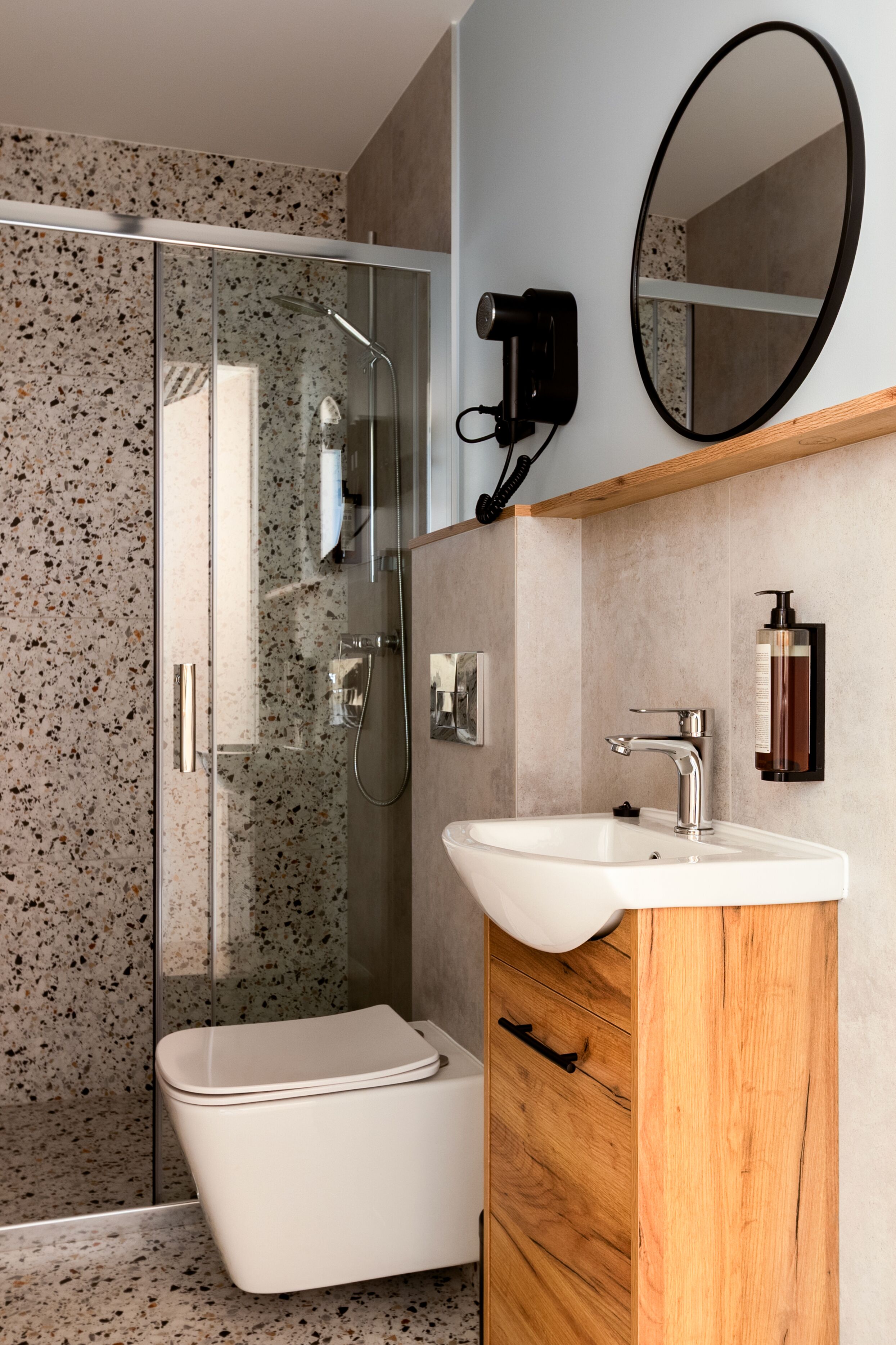 Een moderne badkamer met een glazen douchecabine, een wit toilet, een houten wastafelmeubel met een wastafel en een spiegel.