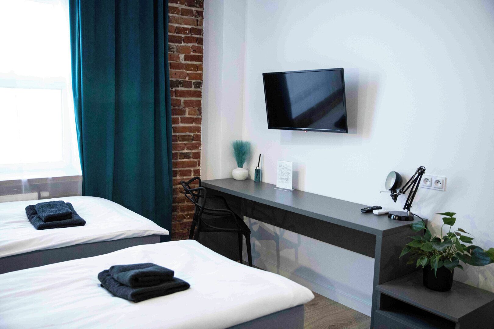 Une chambre d’hôtel avec deux lits, un bureau avec une télévision, une chaise, une lampe de bureau et une plante en pot.