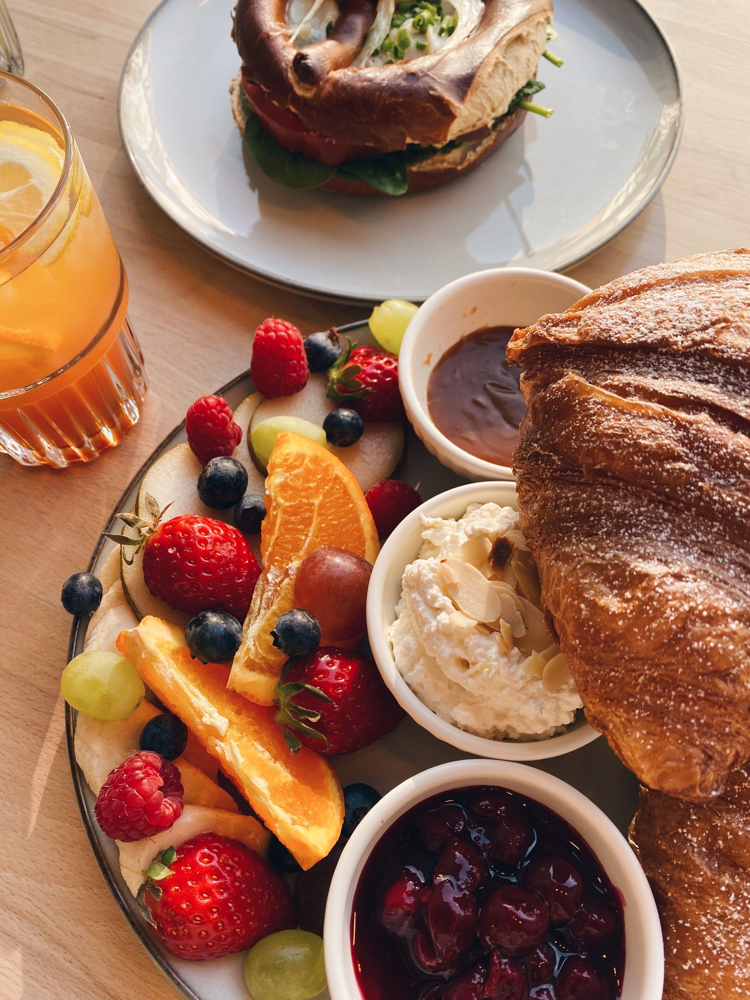 Een ontbijt bord met fruit, een sandwich en een glas sinaasappelsap.