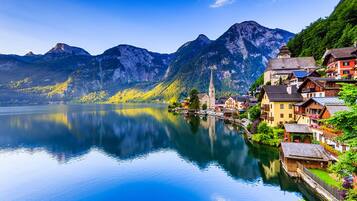 A serene lakeside town with traditional buildings, a church, and mountains in the background.