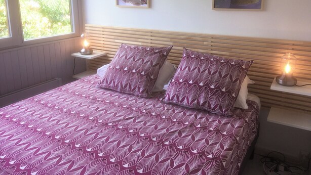 A neatly made bed with patterned bedding, two bedside lamps, and two framed landscape paintings on the wall.