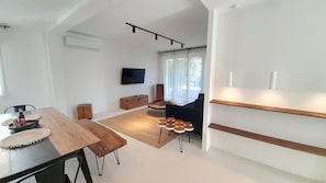 A modern living room with a wooden dining table, a sofa, and a TV mounted on the wall. - Superbe maison 3 chb-clim-jardin-wifi (Châteauroux)