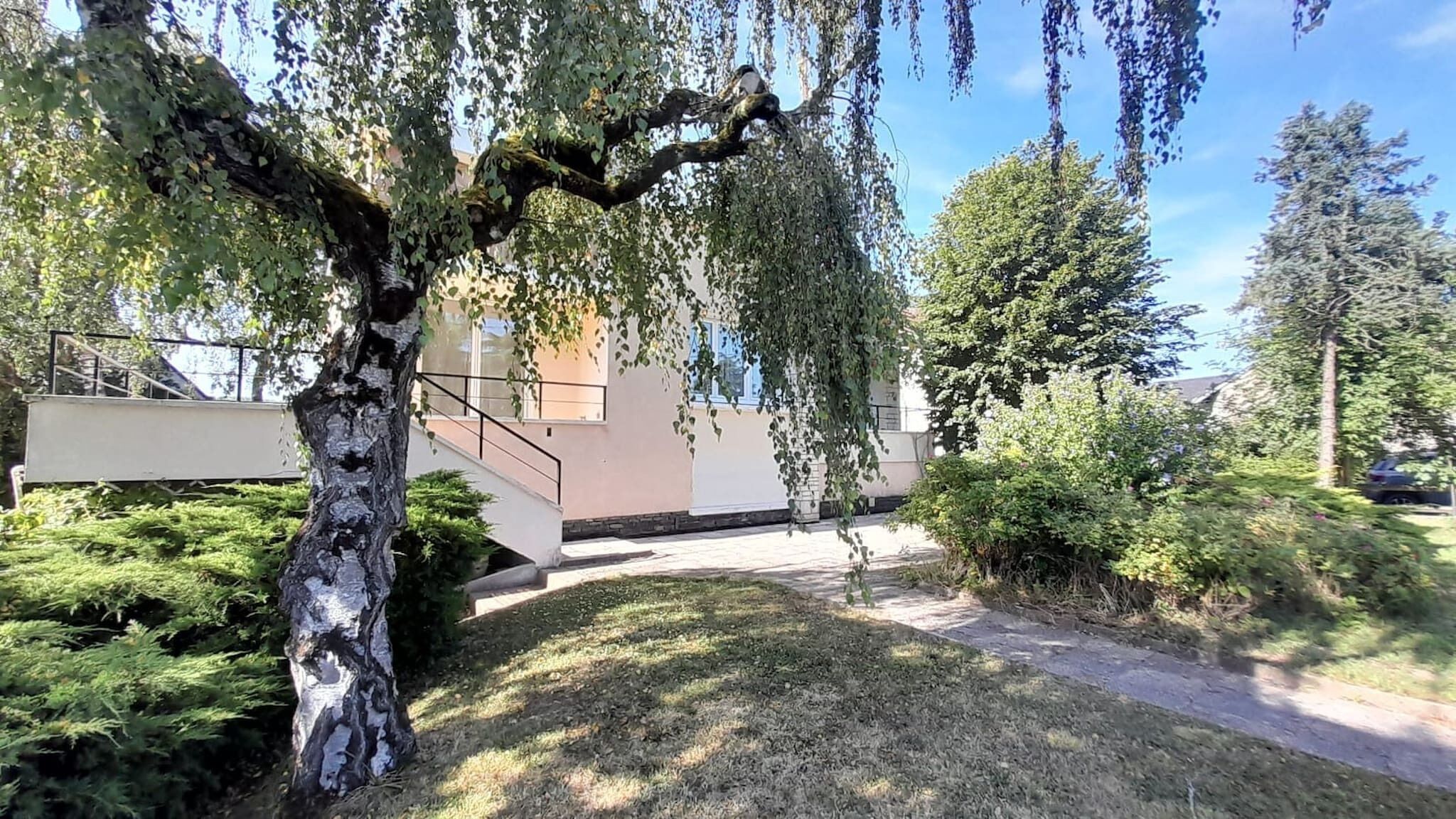 A tree-lined pathway leading to a building with a staircase and a small garden area.