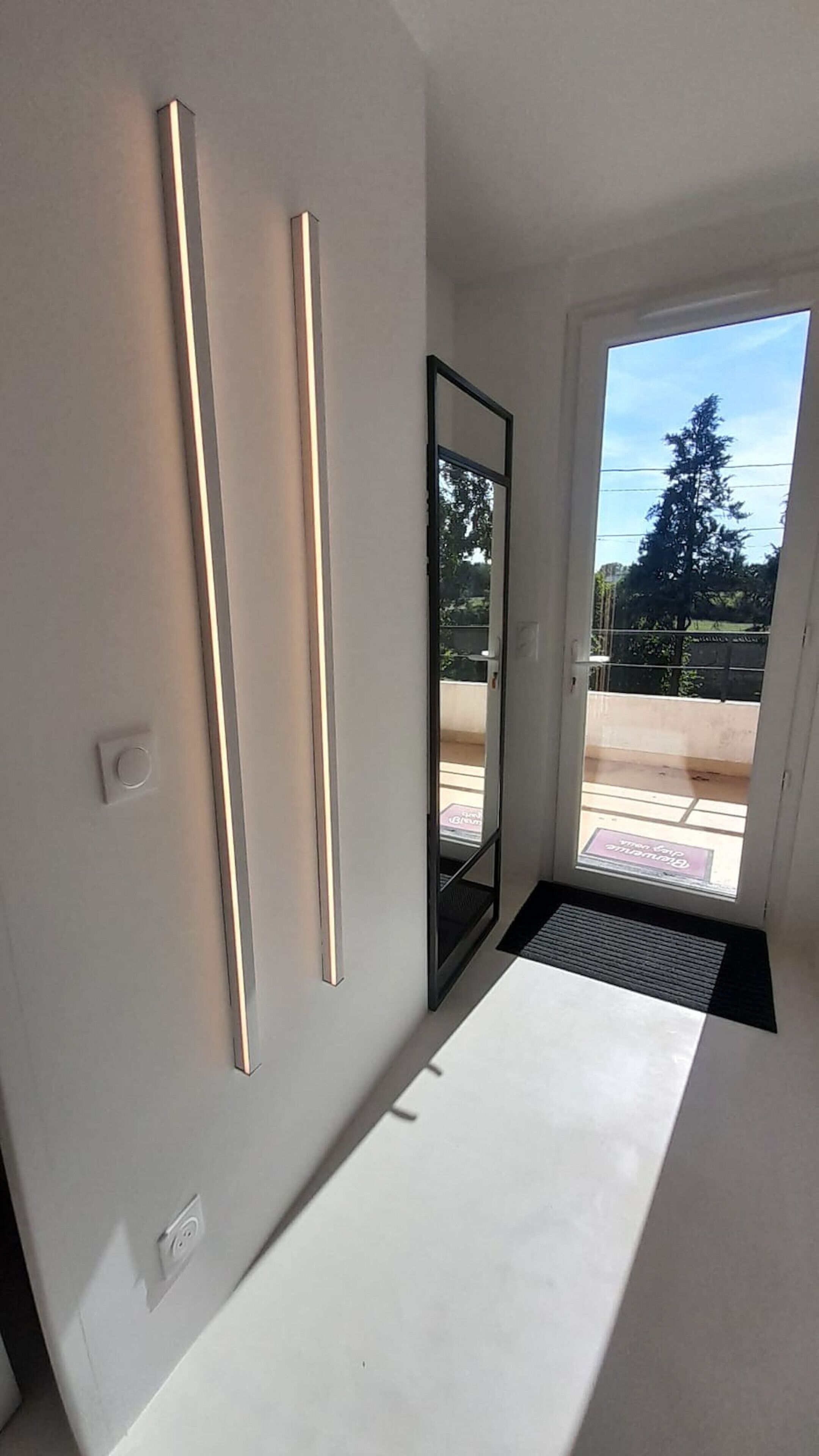 A modern room with a large window, a door, and two vertical light fixtures on the wall.