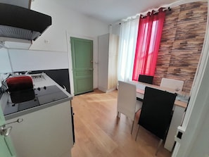 A compact kitchen with a toaster, a green door, a dining area with a table and chairs, and a red curtain. - Appart cosy-4 pers-centre ville-jardin-wifi (Châteauroux)