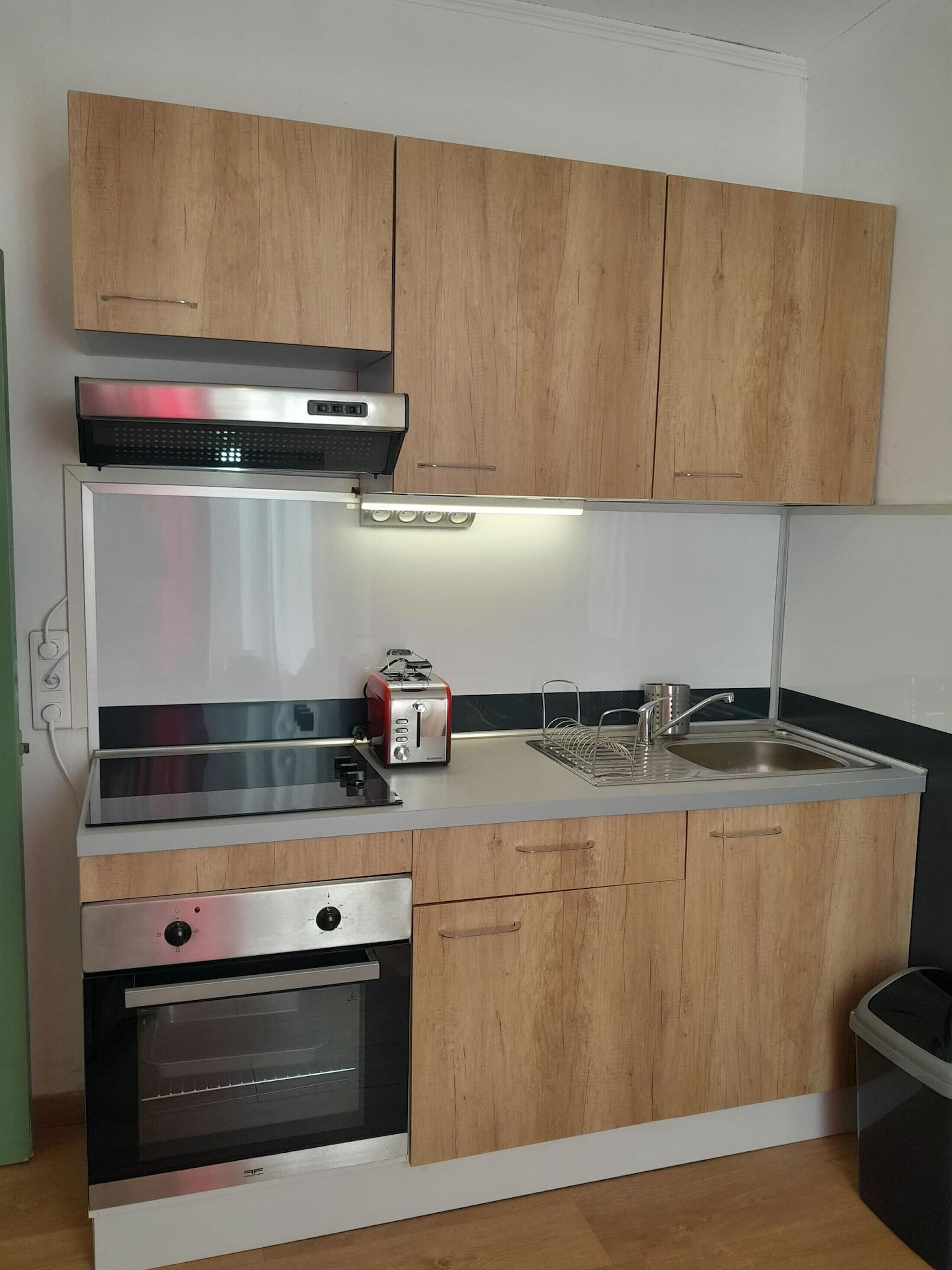 A compact kitchen with wooden cabinets, a built-in oven, a toaster, and a sink.
