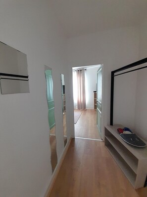 A hallway with a wooden floor, a mirror on the left, and a shoe rack on the right. - Appart cosy-4 pers-centre ville-jardin-wifi (Châteauroux)