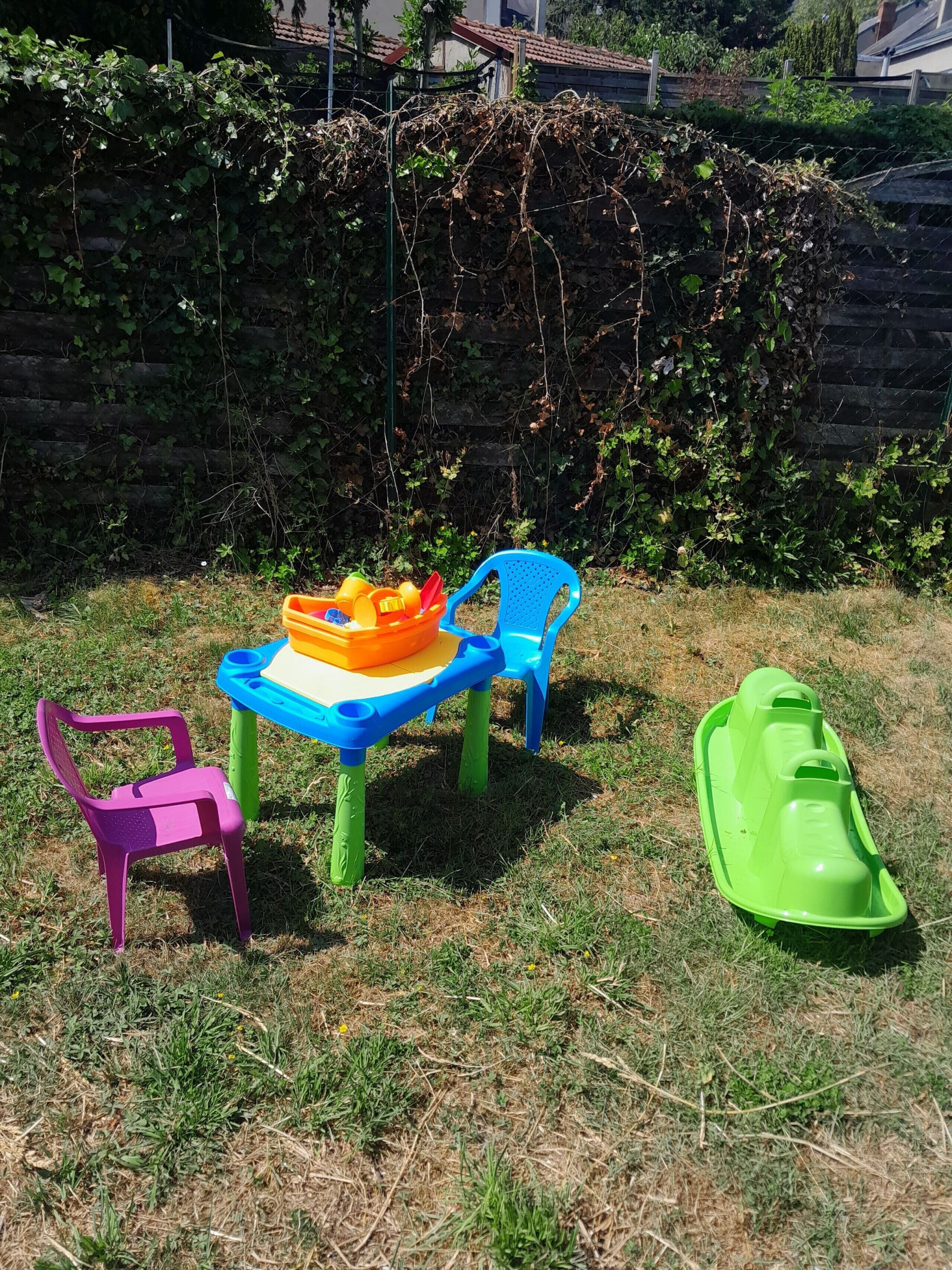 En lekplats för barn med ett bord, två stolar och en liten grön lekanordning.