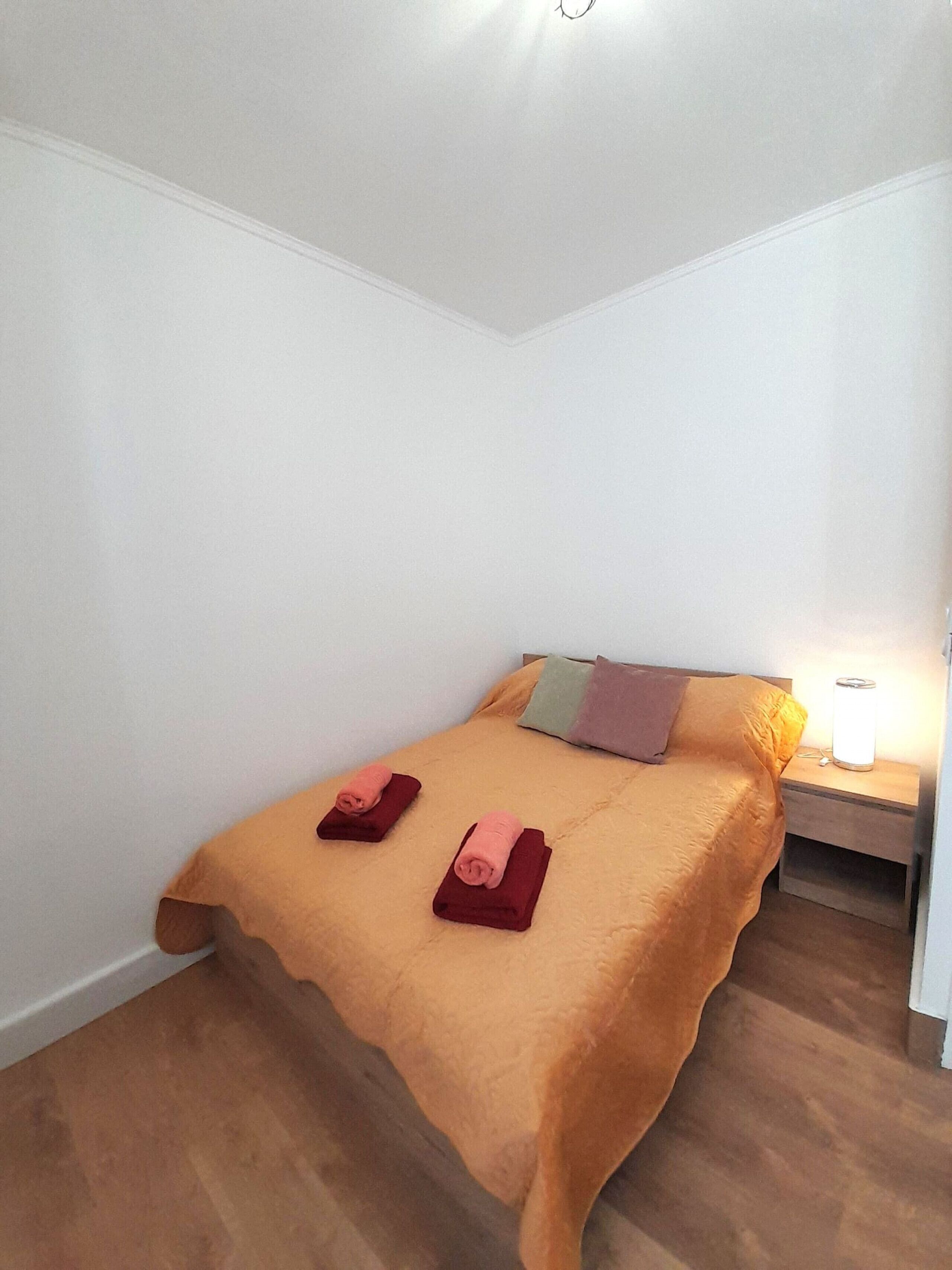 Un letto piccolo e ordinato con copriletto marrone e due asciugamani arrotolati, un comodino con una lampada e un pavimento in legno.