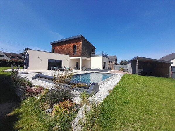 Een modern huis met twee verdiepingen, een zwembad, een overdekt terras en een verzorgd gazon.