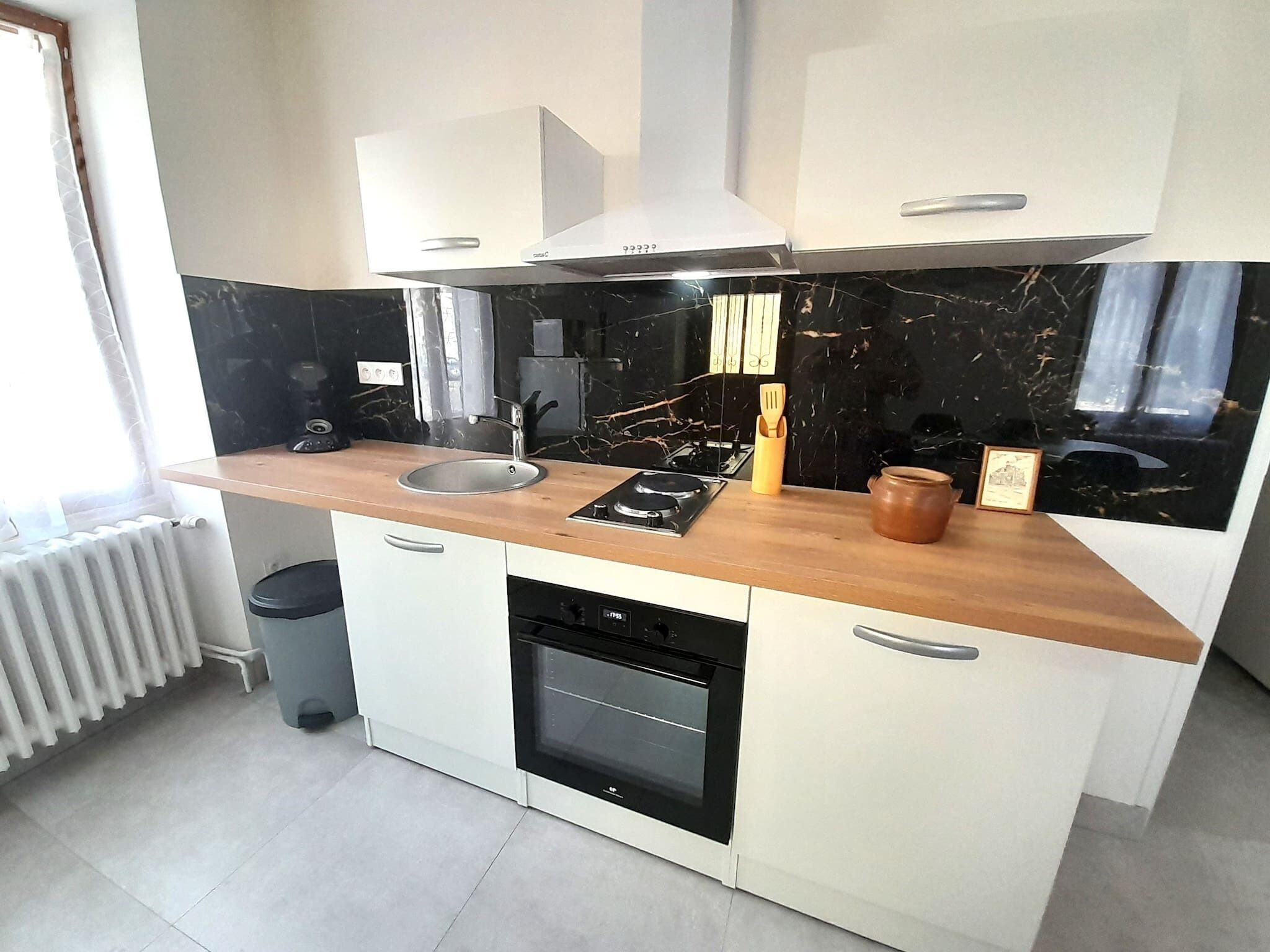A compact kitchen with a black marble backsplash, a wooden countertop, a built-in oven, and a white stove.